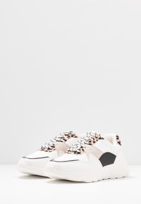 Zapatillas blancas con suela texturizada, acentos de estampado de leopardo y superposiciones negras. Los materiales de piel lisa y ante completan el diseño.