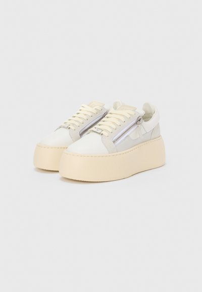 Een paar off-white platform sneakers met dikke beige zolen, crèmekleurige veters en zilveren zijritsen op een effen witte achtergrond.