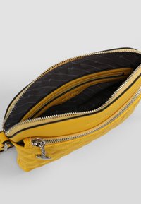 Keltainen nahkainen laukku, jossa on tikattu muotoilu, hopeiset yksityiskohdat, kaksoispussit ja musta sisustus, jossa on hienovarainen kuvio.