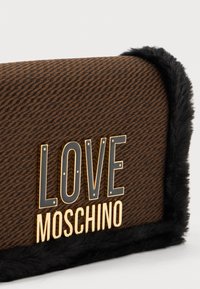 Rjava teksturirana torbica s črnim umetnim krznom. Na sprednji strani se nahajajo zlate črke "LOVE MOSCHINO". Pravokotna oblika.