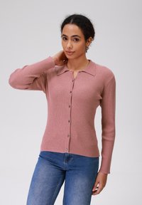 Rožinis raštuotas kardiganas su apykakle, ilgomis rankovėmis ir mygtukų uždarymu priekyje. Minkšta medžiaga ir tekstūruotas paviršius.