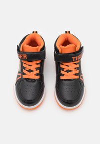 Zapatillas sintéticas negras con acentos naranjas, incluyendo los cordones y una correa, con detalles perforados y una suela blanca. Marca Tiger visible.
