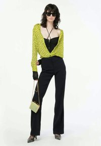 Grön blus med prickar, svart tajt linne, högmidjade svarta byxor, klackskor med silverdetaljer, handväska i guld och grönt, svarta solglasögon, långa ärmar.