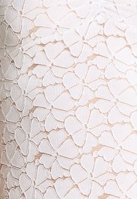 Bílá krajka s květinovým vzorem obsahující srdcovité prvky, která se vyznačuje texturovanou, otevřenou tkaninou a složitými detaily.