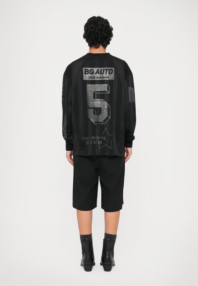 Črn oversized sv sweatshirt z velikim sivim številom 5 in napisom na hrbtu, v kombinaciji s črnimi kratkimi hlačami in ankle škornji.