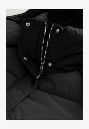 Giacca a vento nera con colletto alto, dotata di una cerniera argentata e bottoni a pressione. Il tessuto ha una consistenza liscia, offrendo isolamento.