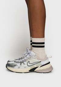 Buty do biegania Nike z szaro-srebrną siateczkową cholewką, czarnymi akcentami i grubą beżową podeszwą. Noszone z kremowymi skarpetami w czarne paski.