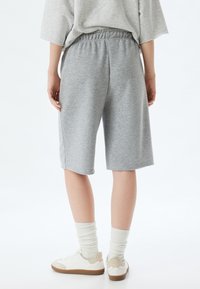 Pantalones cortos de sudadera grises con cintura elástica, de largo hasta la rodilla, con una textura suave. Combinados con zapatillas blancas y calcetas de canalé.