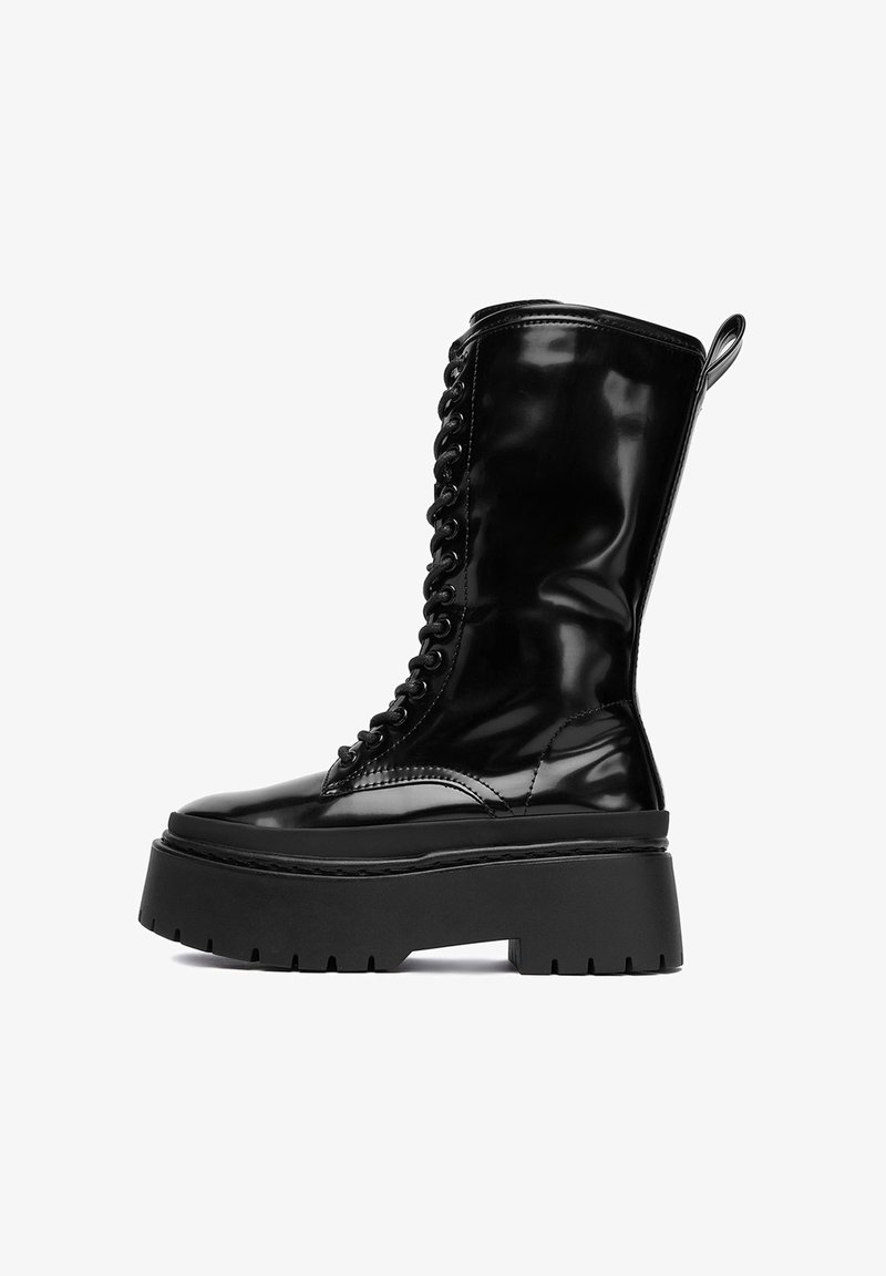 Botine din piele patentă neagră, până la genunchi, cu o talpă groasă neagră, șireturi în față și o buclă în partea de sus pentru o îmbrăcare ușoară.