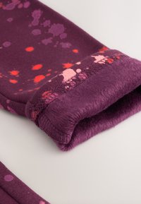 Vijolično oblačilo z žametno podlogo, posuto z roza in rdečimi madeži, s mehkim, teksturiranim manšetom in tesnim oprijemom.