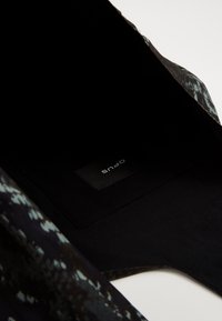 Zwarte binnenkant van een tas met een gladde textuur en een klein label met de tekst "OPUS." De buitenkant toont patronen in donkere tinten.