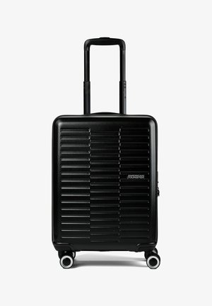 Maleta de mano negra con carcasa dura, estrías horizontales, asa retráctil, cuatro ruedas giratorias y logo de American Tourister en la parte frontal.