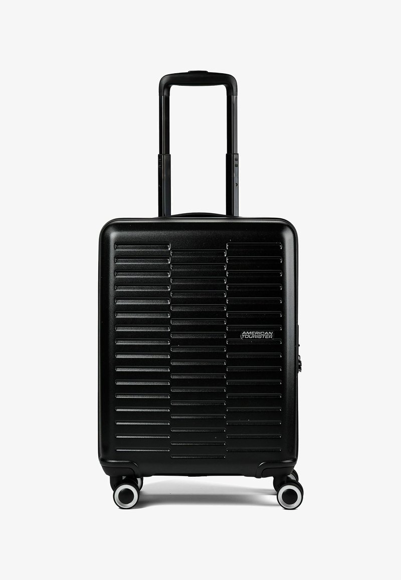 Valise cabine rigide noire avec rainures horizontales, poignée rétractable, quatre roues pivotantes et logo American Tourister à l'avant.