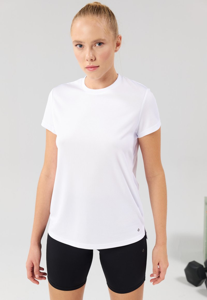 Hvid atletisk T-shirt med korte ærmer og rund hals. Har en blød tekstur og en diskret logoaccent nær kanten.