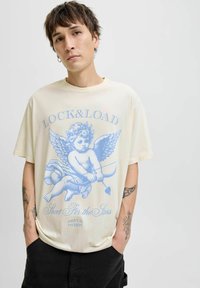 Krémové oversized tričko s modrou grafikou cheruba se šípem a lukem, textem nahoře a dole, a krátkými rukávy.