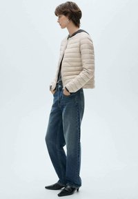 Beige pufferjakke med quiltet design, parret med løstsiddende blå jeans. Sorte spidse sko fuldender outfittet.