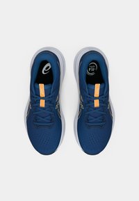 Μπλε αθλητικά παπούτσια με επάνω μέρος από πλέγμα, πορτοκαλί λεπτομέρεια στη γλώσσα και γκρι σόλα. Διαθέτουν υφή στην επιφάνεια και σύστημα κορδονιών.