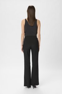 Pantalons évasés taille haute noirs avec une texture lisse, présentant une taille ajustée et une conception de jambe fluide ; associés à un haut sans manches noir.