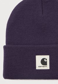 Beret tricotat de culoare purpurie închisă cu manșetă pliată, având o etichetă pătrată albă cu logo-ul Carhartt în negru.