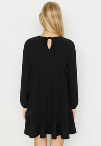 Abito nero a maniche lunghe con design a strati, tessuto strutturato e apertura a chiave sul retro, fissata con un nastro annodato.