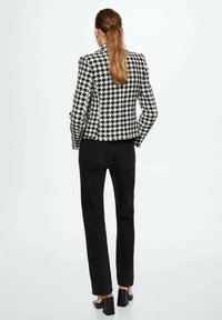 Bunda s dvojbarevným vzorem houndstooth v černobílé, slim fit design, texturovaná látka, kombinovaná s černými kalhotami a botami na blokovém podpatku.