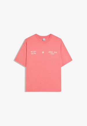 Korallenrosafarbenes T-Shirt mit kurzen Ärmeln und weißem Text "THE BEST ATTITUDE" und "CREATE YOUR STORY", getrennt durch ein kleines Sternsymbol.