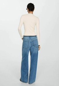 Ribbet, cremet langærmet top med tætsiddende design, parret med lyseblå, brede denimjeans med baglommer og mørkt liv.