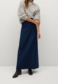 Gonna blu navy, di lunghezza media, realizzata in tessuto morbido, abbinata a un maglione lavorato grigio; modella che indossa stivali neri alla caviglia.