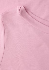 Gros plan sur l'encolure et la couture d'épaule d'un t-shirt en tissu rose doux, avec des coutures visibles et une texture lisse.