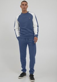 Blue sweatshirt and joggers with white accents, made of soft fabric. Features a round neck, ribbed cuffs, and a small logo on the chest.