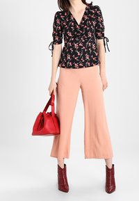 Top nera floreale con maniche corte, abbinato a pantaloni ampi color pesco, borsa a tracolla rossa in pelle e stivaletti ankle in pelle borgogna con borchie.