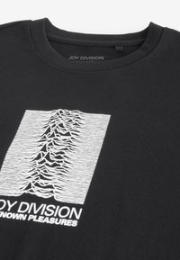 Black cotton t-shirt featuring a white graphic print of jagged lines and text "JOY DIVISION UNKNOWN PLEASURES" underneath. Round neckline.