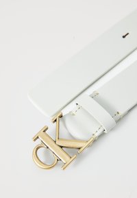 Cinturón de piel blanca con hebilla en tono dorado con el logo CK, diseño elegante con detalles de costura y una textura suave.