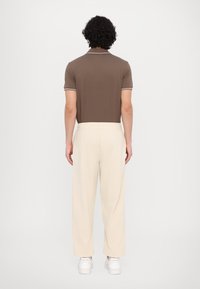 Brown polo shirt with white trim, paired with cream-colored sweatpants. Features a relaxed fit and elastic waist; worn with white sneakers.