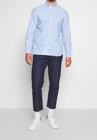 Blue and white striped long-sleeve shirt with a button-down collar, paired with dark denim pants and white sneakers.
