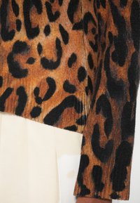 Leopardmönstrad tröja i varma bruna och svarta nyanser, med ribbad textur och rak nederkant, kombinerad med en krämfärgad fabric nedanför.