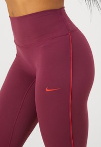 Artimas marškinėlių ir raudonų Nike swoosh logotipų su plona raudona šonine juostele, kurie dėvimi žmogaus.