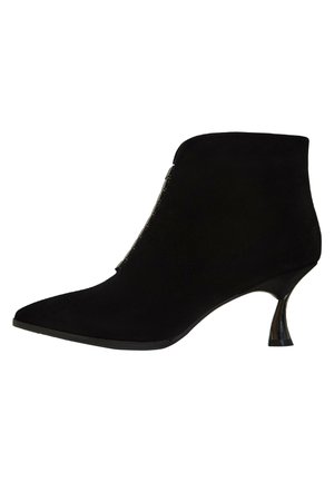 Černá semišová kotníková bota s špičatou špičkou, kovovým bočním zipem a zakřiveným jehlovým podpatkem. Hladká textura, minimalistický design.