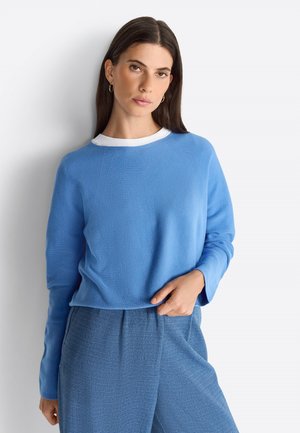 Maglione azzurro chiaro in tessuto strutturato con colletto girocollo bianco, abbinato a pantaloni blu a fantasia; vestibilità morbida e maniche lunghe.