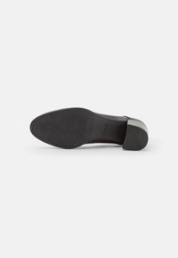 Suola di scarpa nera con motivo di grip texturizzato; presenta un tacco basso a blocco e un design curvo e liscio sulla parte superiore. Logo del marchio visibile.