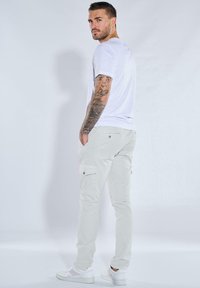 Weißes T-Shirt kombiniert mit hellgrauen Cargo-Hosen, die seitliche Taschen und ein Knopfdetail aufweisen, abgerundet mit weißen Turnschuhen. Glatte Texturen durchgehend.