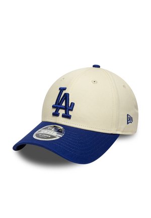 Gorra de béisbol de tela crema con visera azul. Lleva un logo "LA" azul bordado en la parte delantera y una etiqueta circular en la visera.