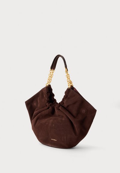 Sac à main en daim marron doux avec poignées chaîne dorée et détail froncé sur le dessus, posé sur un fond clair uni.