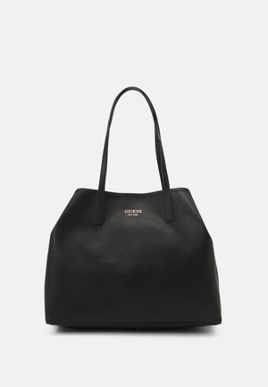 Sac à main en cuir noir texturé avec deux bretelles et logo doré "GUESS EST 1981" centré près du haut.