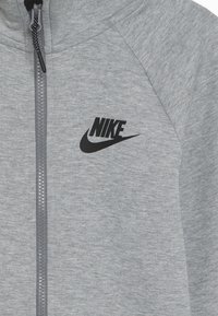 Grå zip-up sweatshirt i mjukt material. Har en svart Nike-logga på vänster bröst och kontrasterande dragkedja. Texturerad yta.