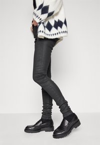 Jeans skinnies negros de denim, con una textura suave. Combinados con zapatos negros de plataforma y un suéter blanco con patrones de rombos azules.