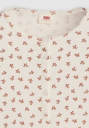 White cotton top featuring a round neckline, vertical ribbing, small floral print in rust color, and five decorative buttons down the center.