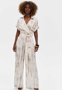 Lichte beige jumpsuit met een wikkeldesign, korte mouwen en een ceintuurlijn in de taille. Heeft een gestructureerd gestreept patroon over het geheel.