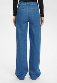 Wide-leg denim trousers in medium blue with a smooth texture. Features two back pockets and a high waist design.