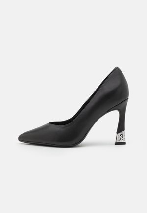 Scarpa con tacco alto in pelle nera, con punta affilata e un accento decorativo in argento sul tallone. Texture liscia e design elegante.